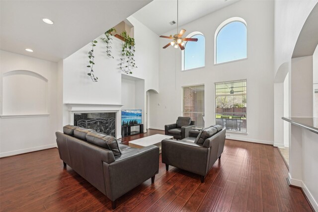 living room featuring arched walkways, a healthy amount of sunlight, a ceiling fan, and dark wood-style flooring