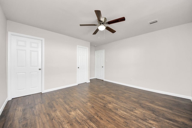 empty room featuring visible vents, a ceiling fan, dark wood-type flooring, and baseboards