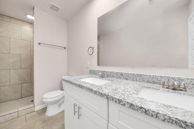 bathroom featuring visible vents, toilet, double vanity, a tile shower, and a sink