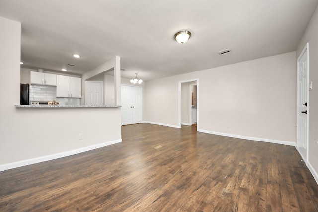 unfurnished living room featuring dark wood-style floors, visible vents, a chandelier, and baseboards