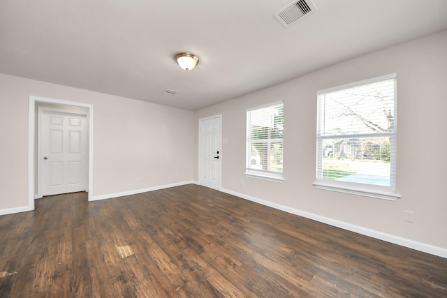 empty room featuring visible vents, baseboards, and dark wood finished floors