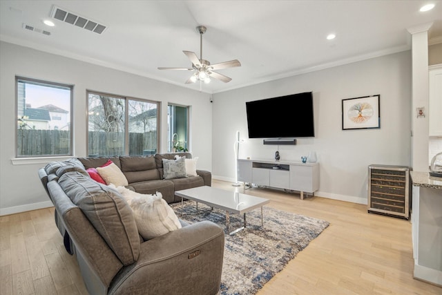 living area featuring visible vents, wine cooler, light wood-type flooring, ornamental molding, and a ceiling fan