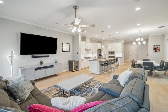 living room featuring ceiling fan with notable chandelier, recessed lighting, light wood-style floors, crown molding, and baseboards