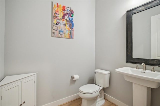 half bathroom featuring toilet, wood finished floors, baseboards, and a sink