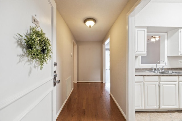 hallway with a sink, visible vents, light wood-type flooring, and baseboards