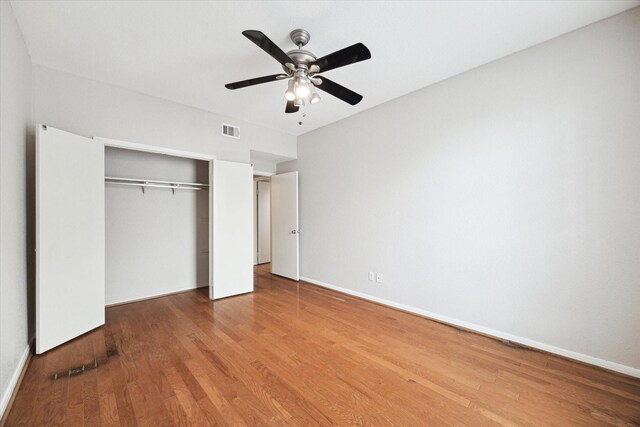 unfurnished bedroom with wood finished floors, visible vents, baseboards, ceiling fan, and a closet