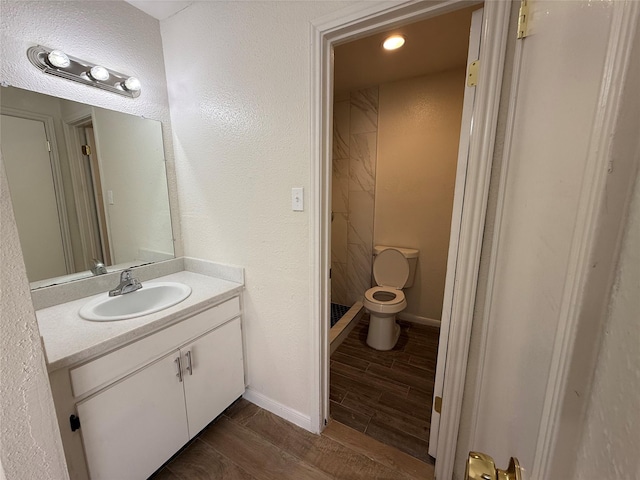 bathroom with a shower stall, baseboards, wood finish floors, toilet, and vanity