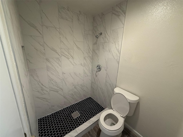 bathroom with a shower stall, toilet, baseboards, and a textured wall