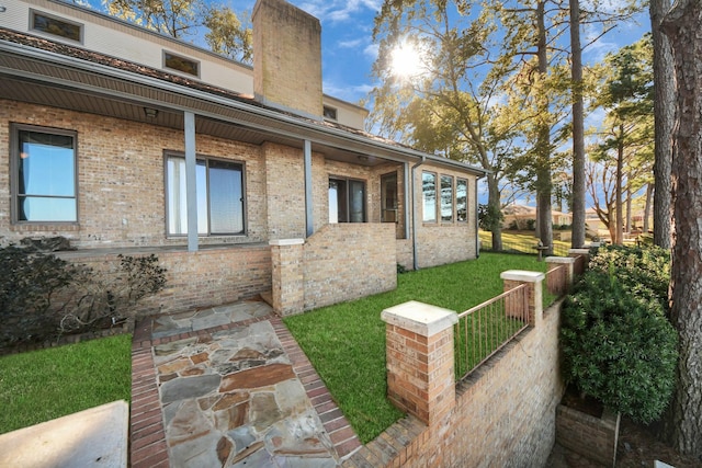 exterior space featuring brick siding, a chimney, a yard, and fence