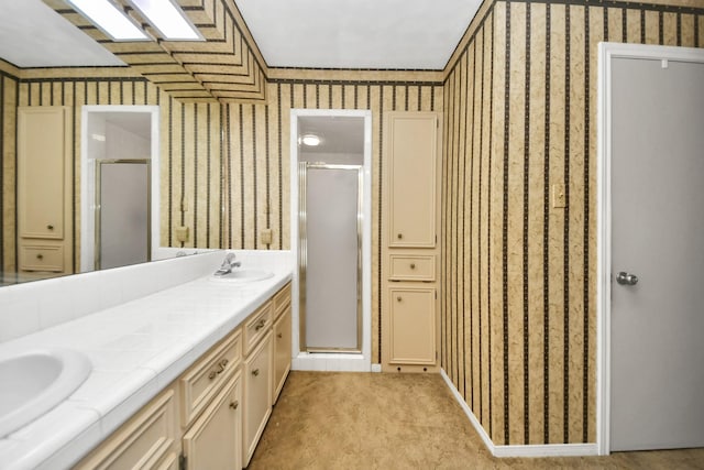 bathroom featuring double vanity, a sink, a shower stall, and wallpapered walls