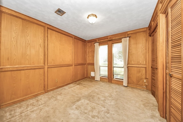 empty room featuring wooden walls, visible vents, and light carpet