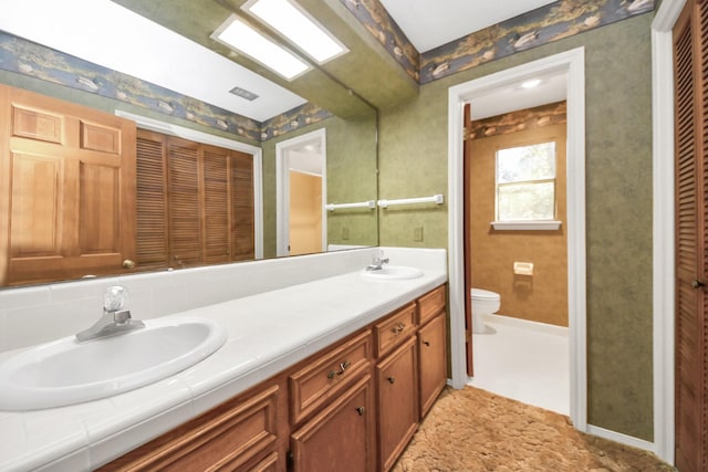 bathroom with wallpapered walls, double vanity, a sink, a closet, and toilet