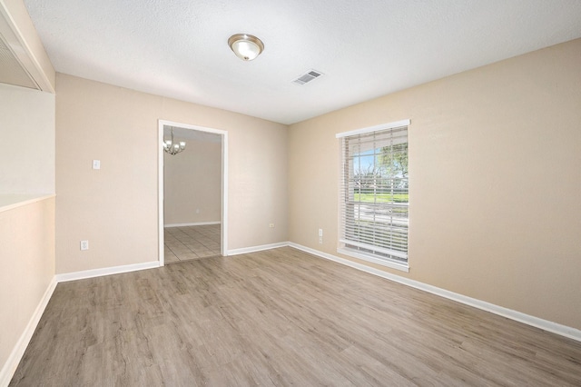 empty room featuring visible vents, an inviting chandelier, baseboards, and wood finished floors