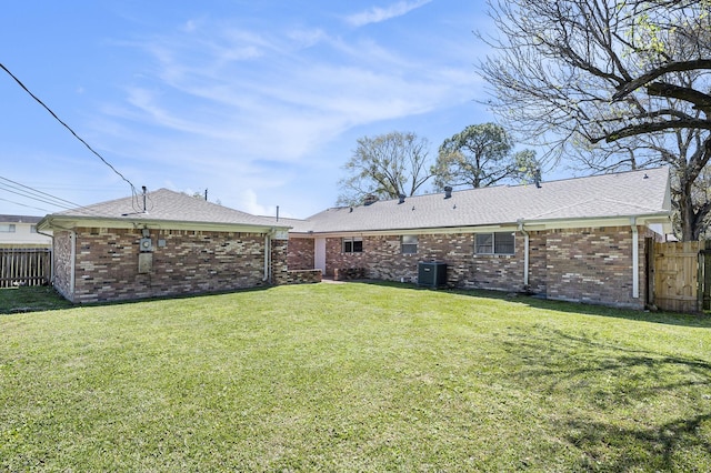 rear view of house with a yard, fence, and brick siding