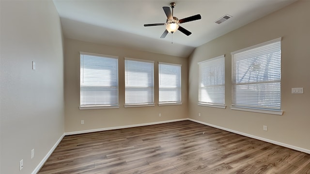 empty room with a ceiling fan, wood finished floors, visible vents, and baseboards