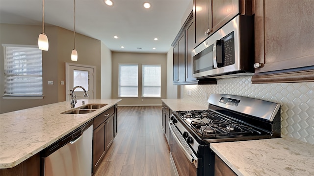 kitchen with backsplash, light stone countertops, appliances with stainless steel finishes, wood finished floors, and a sink