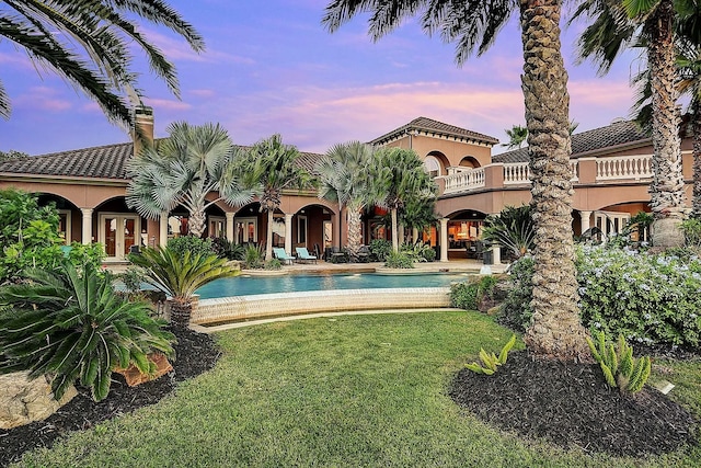 rear view of house featuring stucco siding, a lawn, a balcony, an outdoor pool, and a patio