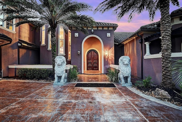 exterior entry at dusk with stucco siding and a tiled roof