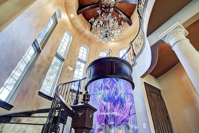 staircase with decorative columns, a textured wall, a towering ceiling, and a chandelier