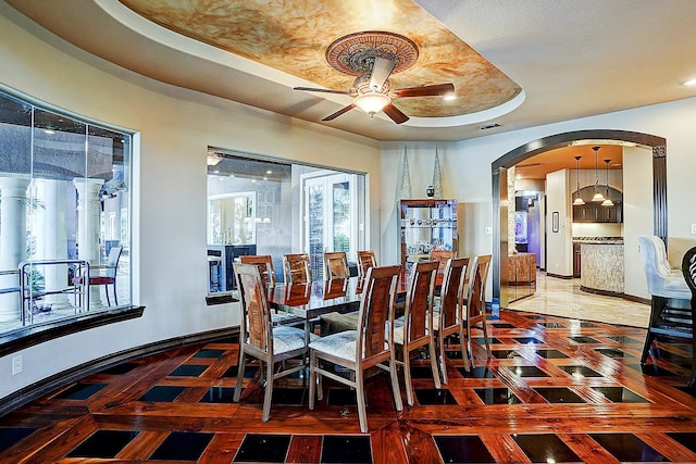 dining area with arched walkways, visible vents, a raised ceiling, and baseboards