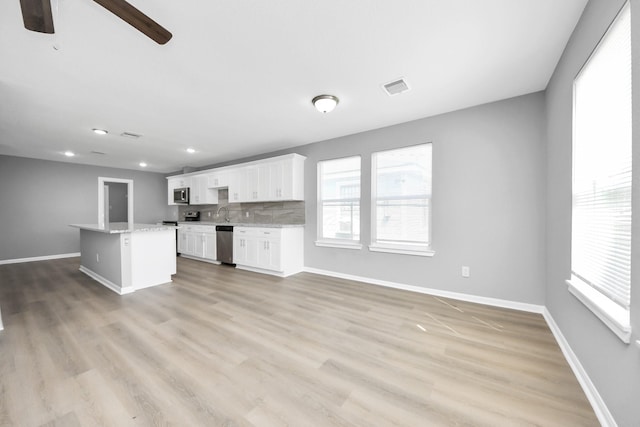 kitchen with baseboards, visible vents, a kitchen island, decorative backsplash, and appliances with stainless steel finishes