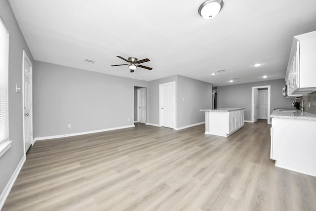 unfurnished living room with a sink, baseboards, light wood-style floors, and ceiling fan