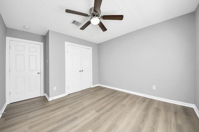 unfurnished bedroom featuring wood finished floors, visible vents, baseboards, ceiling fan, and a closet