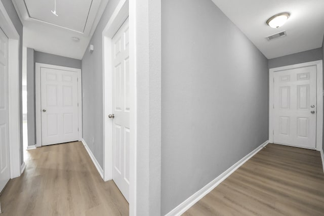 corridor with attic access, wood finished floors, visible vents, and baseboards