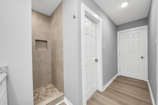 bathroom featuring wood finished floors, baseboards, and a tile shower