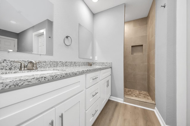 bathroom featuring double vanity, wood finished floors, a walk in shower, and a sink