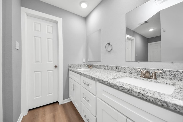 full bath featuring double vanity, wood finished floors, baseboards, and a sink