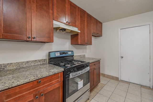 kitchen with under cabinet range hood, light stone counters, light tile patterned floors, baseboards, and stainless steel range with gas stovetop