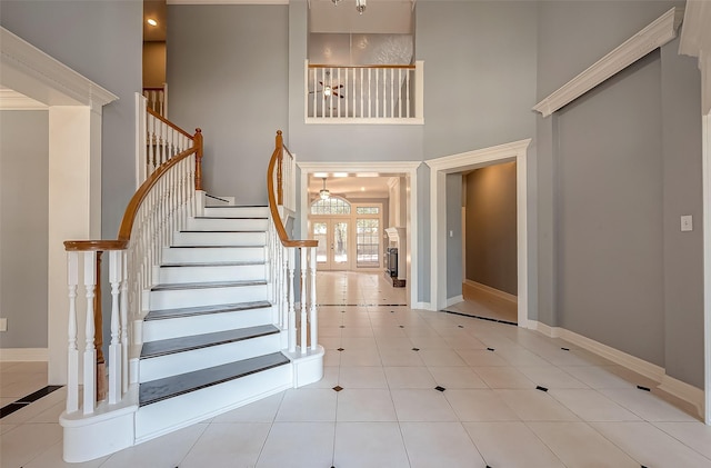 tiled entrance foyer with french doors, baseboards, a towering ceiling, and stairs