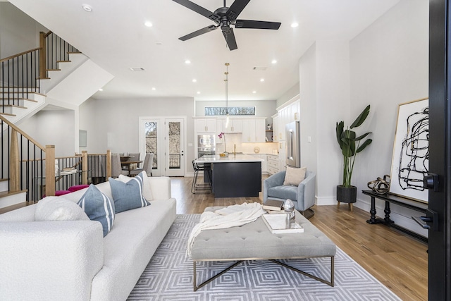 living room featuring recessed lighting, baseboards, light wood-style floors, and stairs