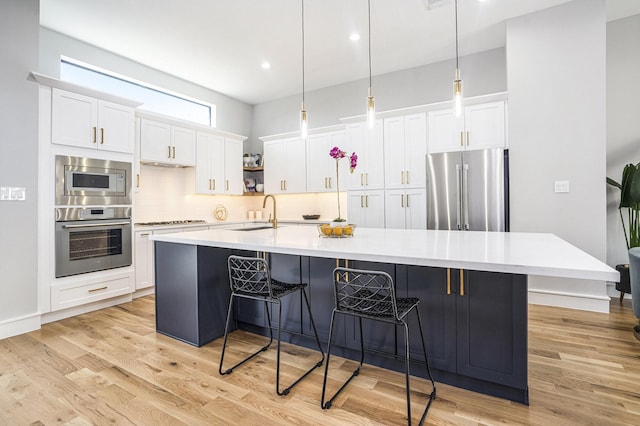 kitchen featuring a sink, backsplash, stainless steel appliances, light wood-style floors, and a large island with sink