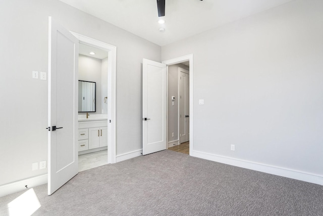 unfurnished bedroom with baseboards, light colored carpet, ensuite bath, and a ceiling fan