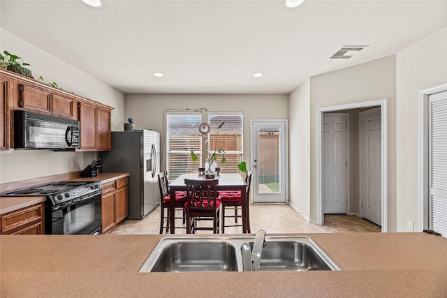 kitchen featuring black appliances, brown cabinetry, visible vents, and a sink