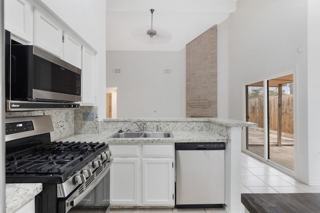 kitchen featuring light tile patterned floors, a peninsula, a sink, white cabinets, and appliances with stainless steel finishes