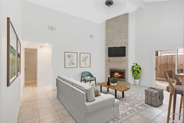 living area with light tile patterned flooring, visible vents, a fireplace, and high vaulted ceiling