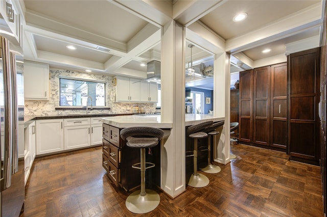 kitchen featuring beam ceiling, a sink, coffered ceiling, white cabinetry, and a breakfast bar area