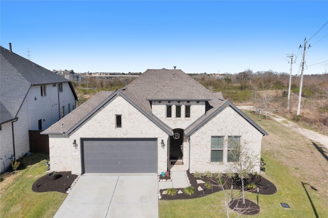 french country inspired facade with a front yard, roof with shingles, an attached garage, concrete driveway, and brick siding