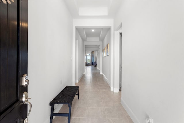 hall featuring light tile patterned floors, baseboards, and a raised ceiling