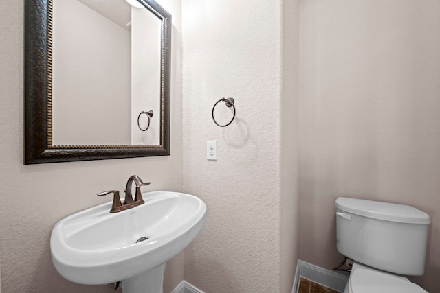 bathroom with toilet, a textured wall, baseboards, and a sink