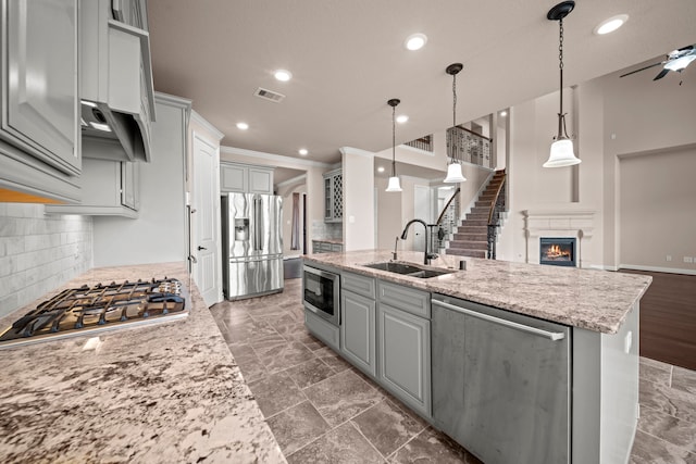 kitchen featuring visible vents, a sink, a warm lit fireplace, stainless steel appliances, and a kitchen island with sink