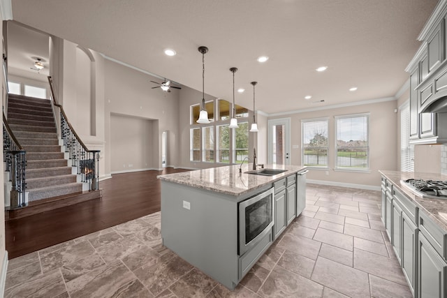 kitchen with a center island with sink, gray cabinets, a sink, appliances with stainless steel finishes, and crown molding