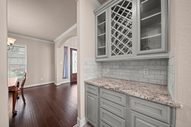 kitchen featuring glass insert cabinets, arched walkways, ornamental molding, and gray cabinets