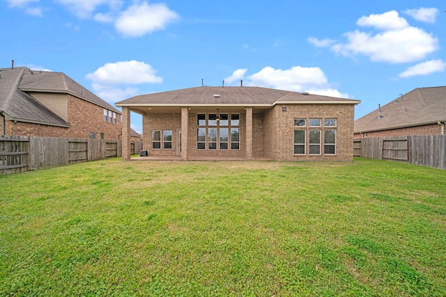 rear view of property with brick siding, a fenced backyard, and a lawn