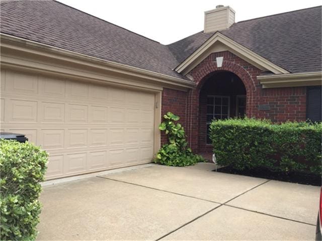 exterior space featuring concrete driveway, brick siding, and a shingled roof