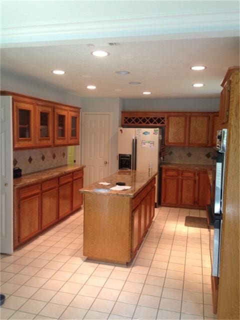 kitchen featuring brown cabinetry, decorative backsplash, a kitchen island, and white fridge with ice dispenser