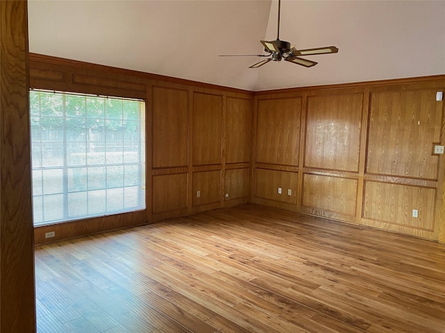 spare room featuring light wood-type flooring, wood walls, a ceiling fan, and vaulted ceiling